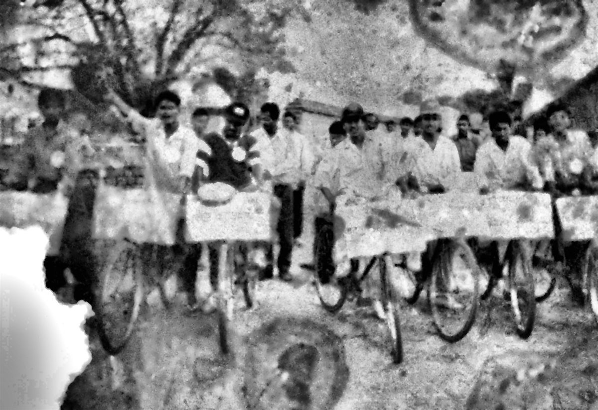 Restored monochrome photograph of a bicycle awareness rally with volunteers carrying hand-painted banners.