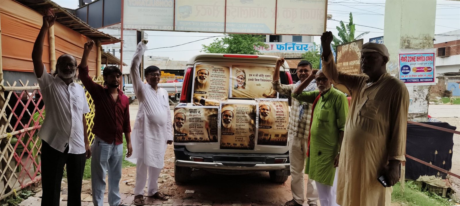 Samiti members with raised fists beside a vehicle covered in posters carrying poems by Nagarjun and Kabir, June 2026.