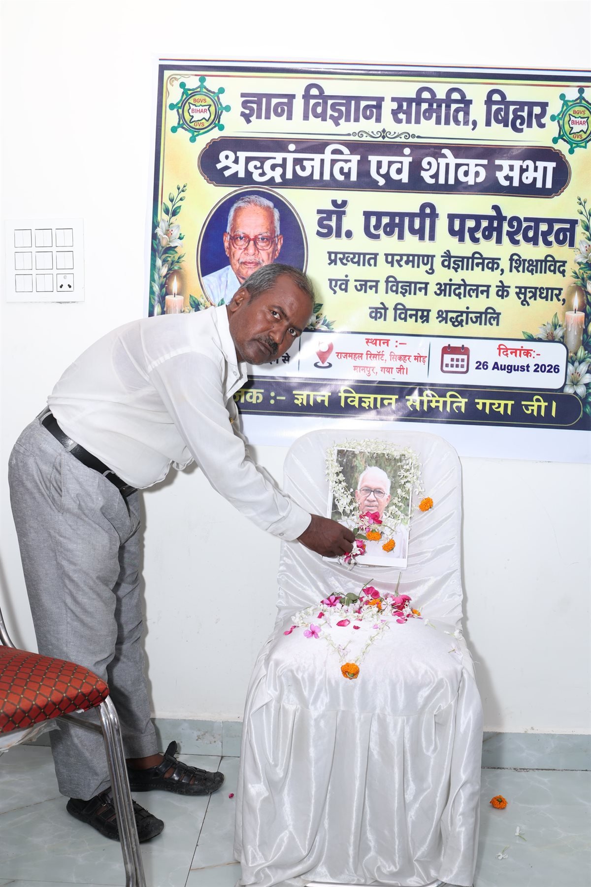 A samiti member places flowers before a garlanded portrait of Dr M.P. Parameswaran at a tribute meeting in Manpur, Gaya, August 2026.
