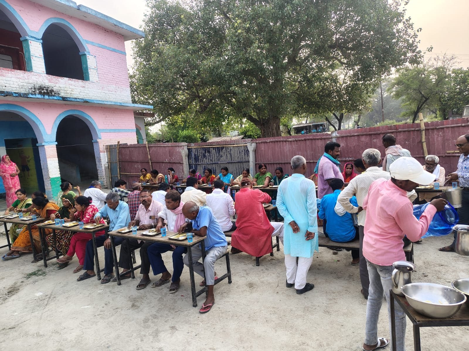 Participants at a samiti training camp eating together at benches in a school compound, Begusarai, June 2026.